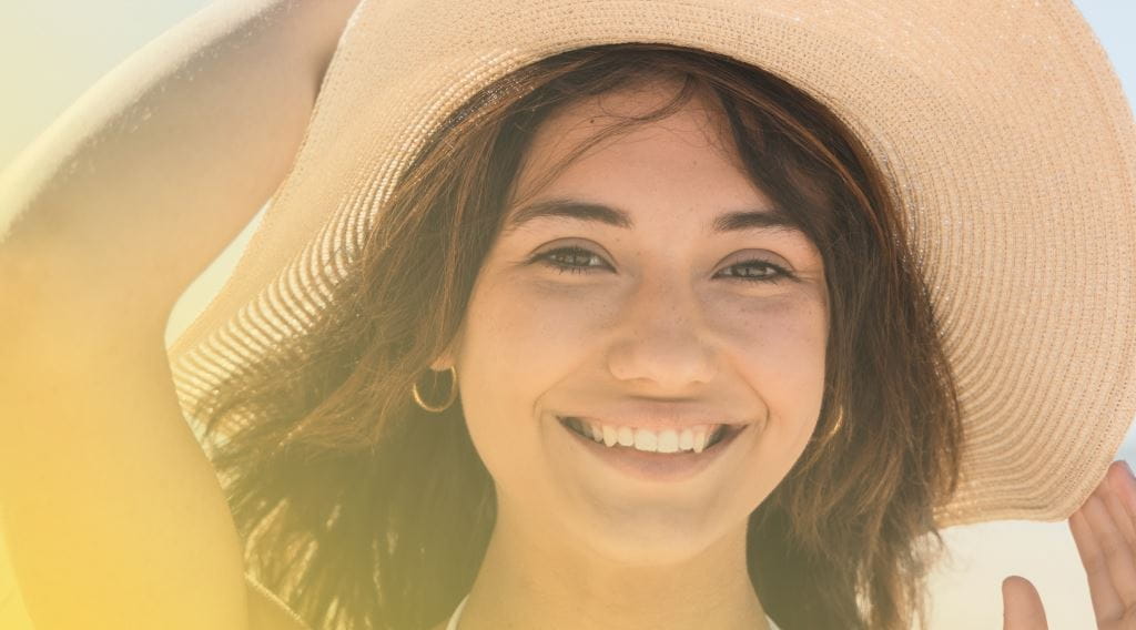 Smiling woman holding her hat at the beach