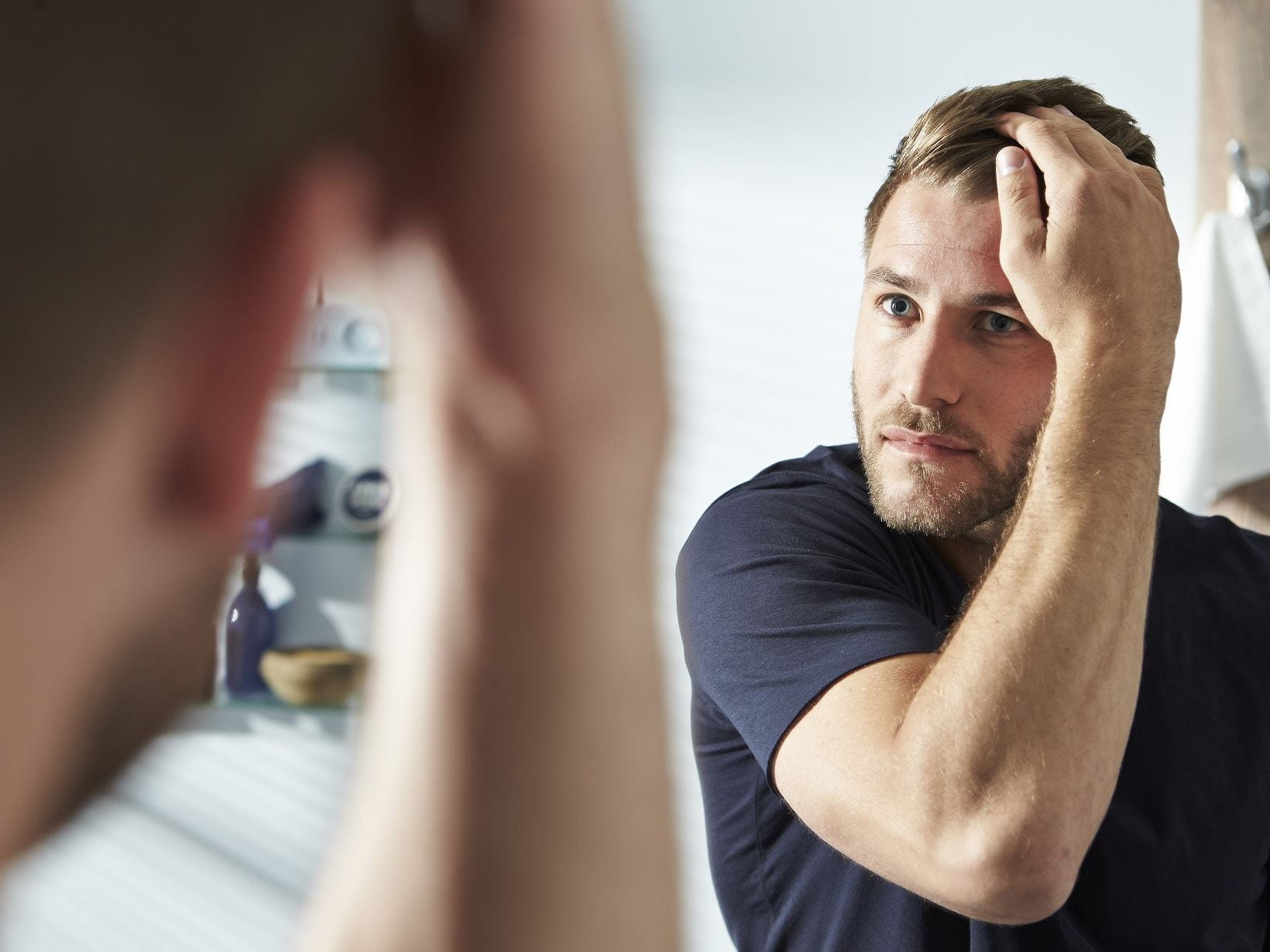 blonde haired man getting rid of his dandruff in front of a mirror