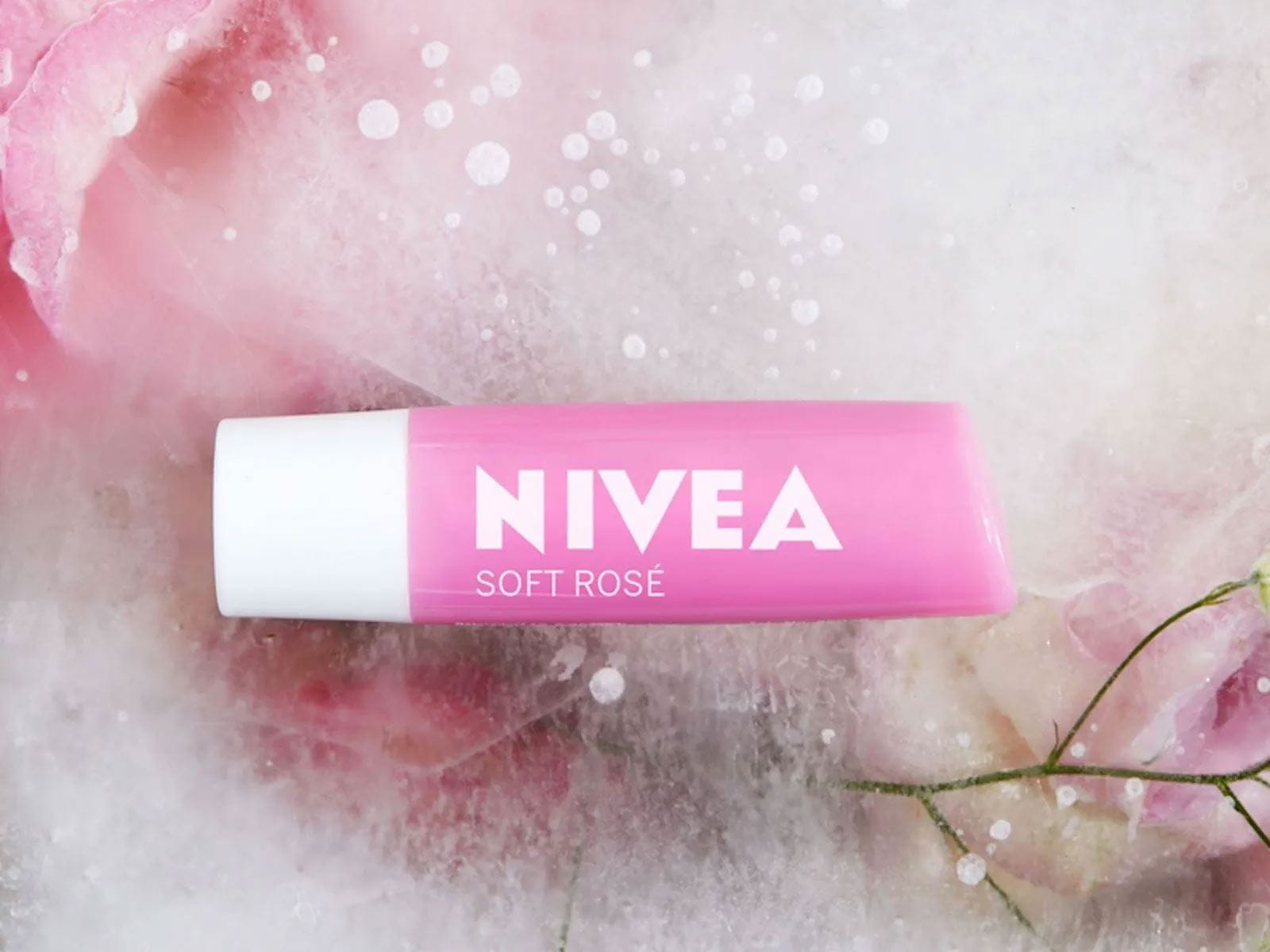View of a Nivea Watermelon Shine Duo Lip Balm product overtop a rose petal covered background.